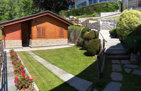 A fianco di una scalinata in pietra cinta da aiuole che porta al ristorante La Bossola c'è lo Chalet Vacanza Menabrea. La struttura è in legno con un muretto decorativo alla sua base, di fronte allo chalet un ampio prato con erba rasata e fiori.